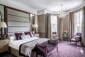 A hotel room with a large bed, two chairs, a small table, and a chandelier. - Woodlands Park Hotel (Cobham)