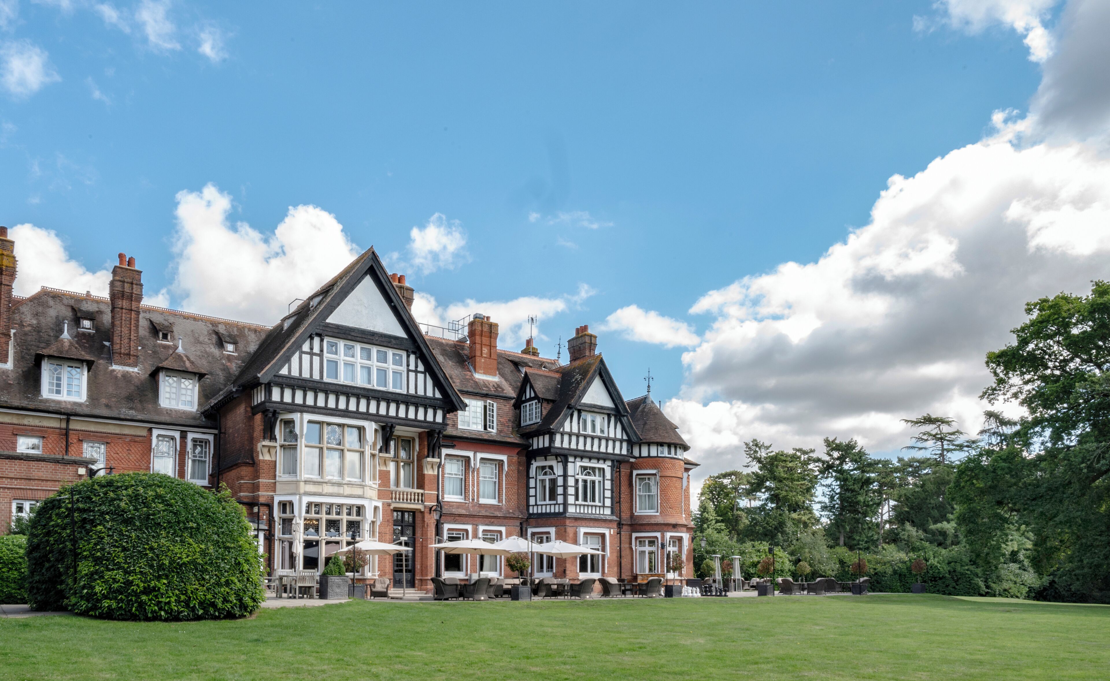 A large, historic building with multiple stories, a prominent chimney, and a well-maintained lawn with outdoor seating.