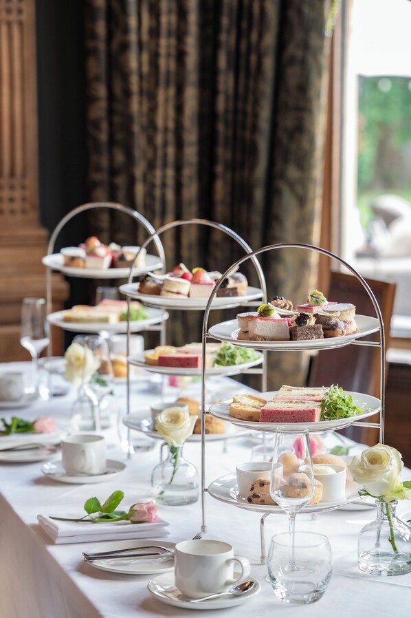 A multi-tiered dessert stand with various pastries and sandwiches, set on a table with white tablecloths and floral decorations. - Woodlands Park Hotel (Cobham)
