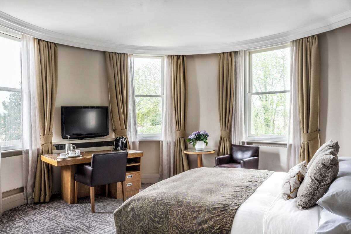 A hotel room with a bed, a desk with a chair, a television, and a small table with a vase of flowers.