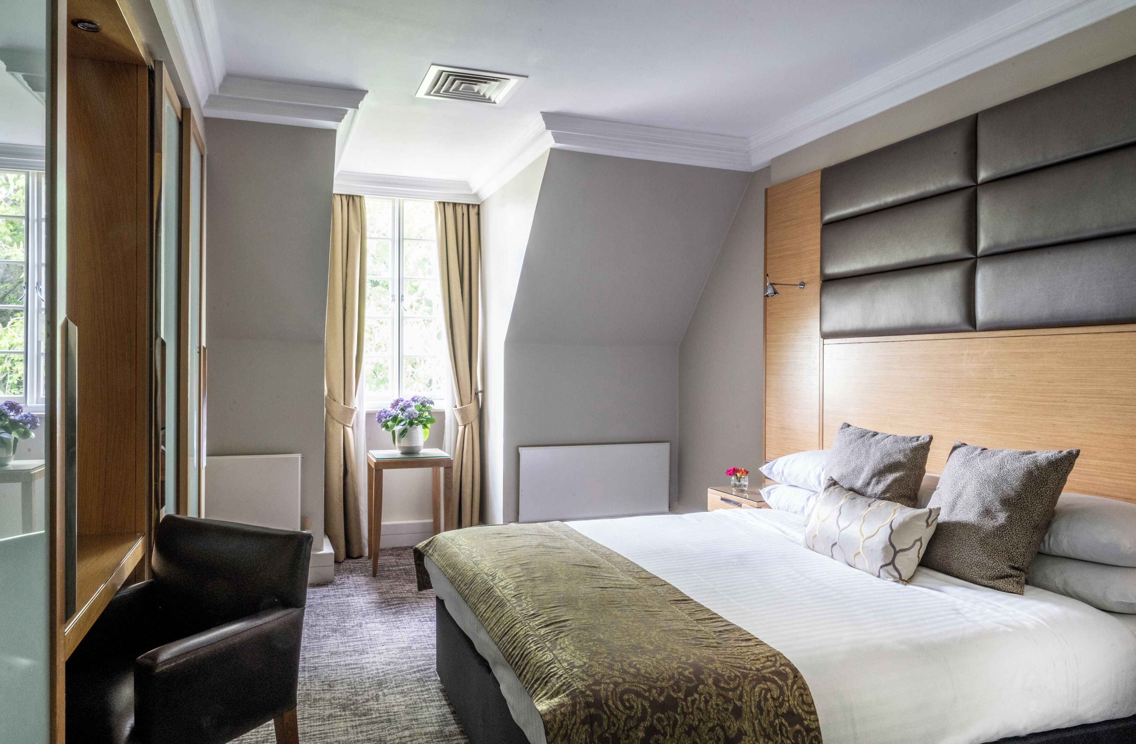 Une chambre d’hôtel avec un grand lit, un bureau, une chaise, une fenêtre avec des rideaux et un radiateur.