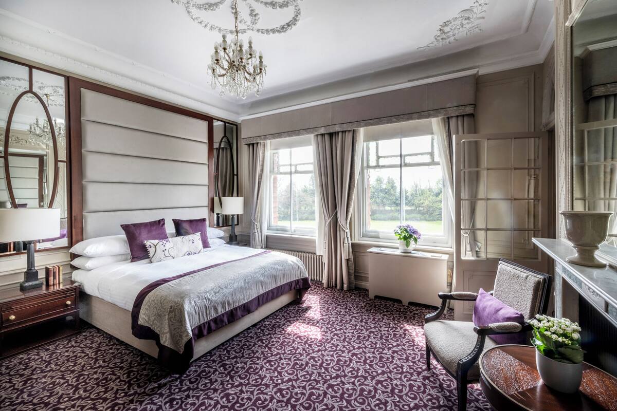 A well-appointed bedroom with a large bed, a sitting area with a chair, and a view through the window.