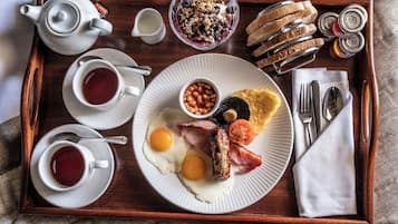 A breakfast tray with eggs, sausage, bacon, toast, jam, and a teapot.