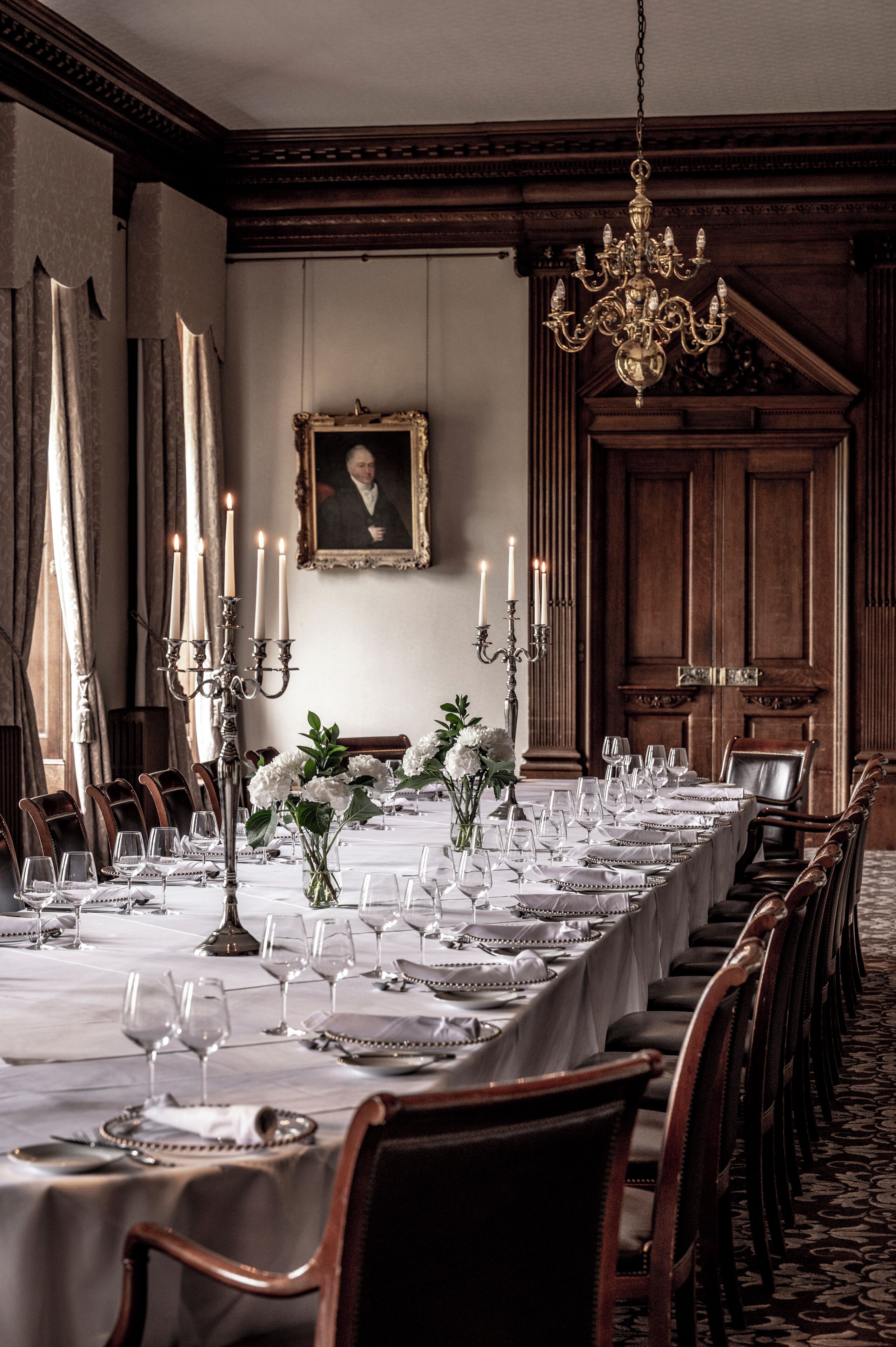 Un comedor formal con una larga mesa dispuesta para una comida, rodeada de sillas de madera.