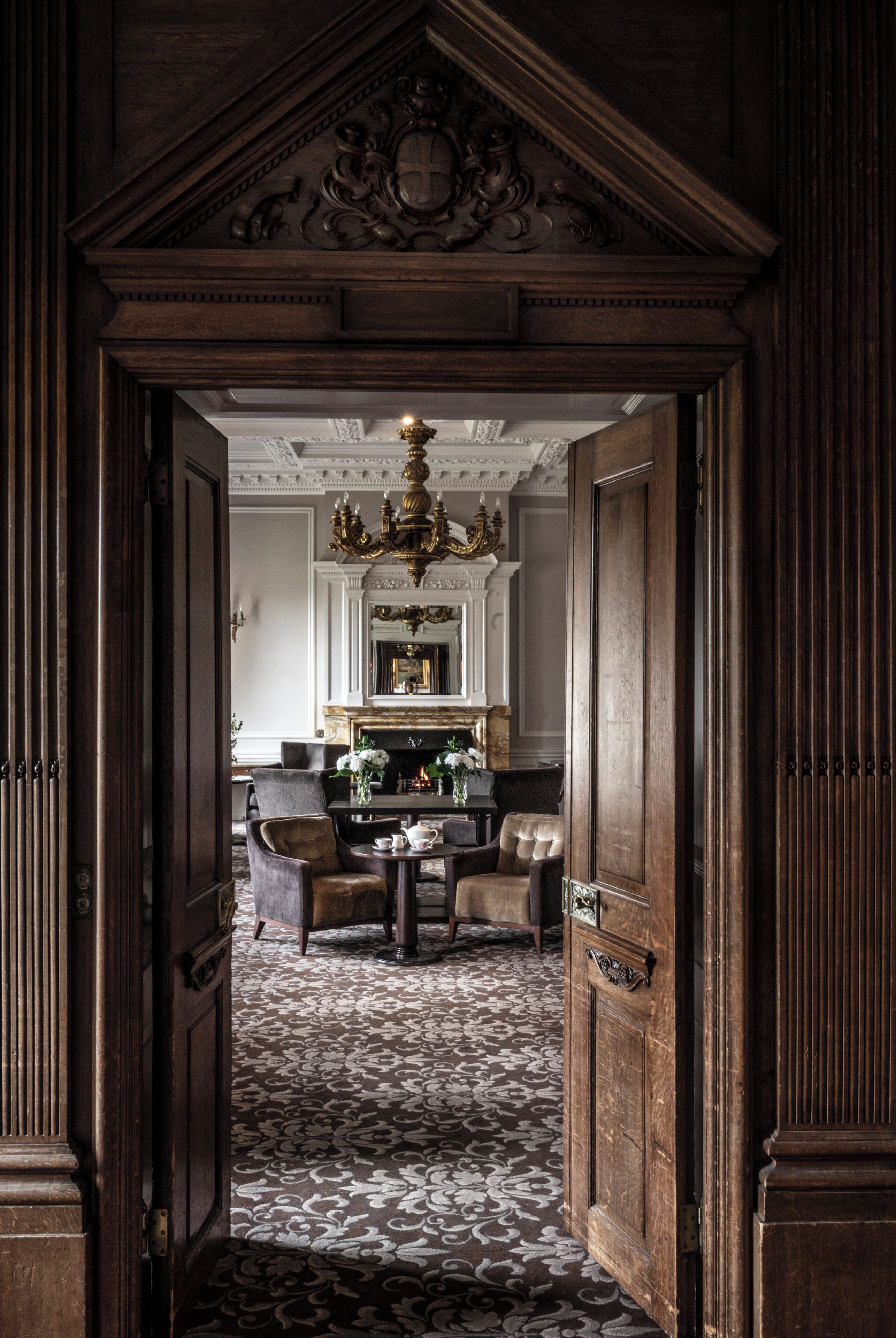 An ornate doorway leading to a room with a patterned carpet, a chandelier, and a fireplace.