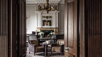 An ornate doorway leading to a room with a patterned carpet, a chandelier, and a fireplace.