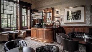 A bar area with a wooden counter, bar stools, and a seating area with leather chairs and a sofa. - Crathorne Hall Hotel (Yarm)