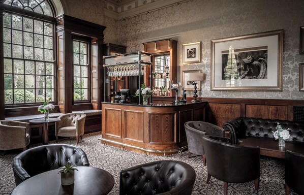 A bar area with a wooden counter, bar stools, and a seating area with leather chairs and a sofa. - Crathorne Hall Hotel (Yarm)