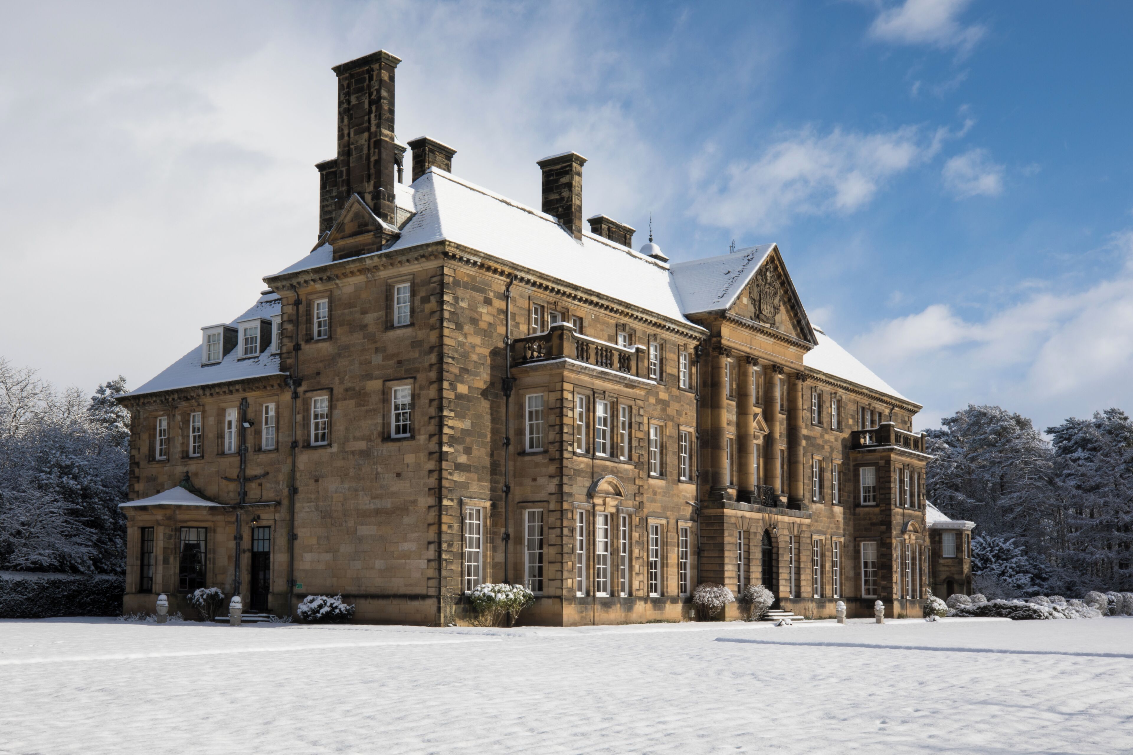 A large, historic building with multiple chimneys, a snow-covered roof, and a symmetrical facade.