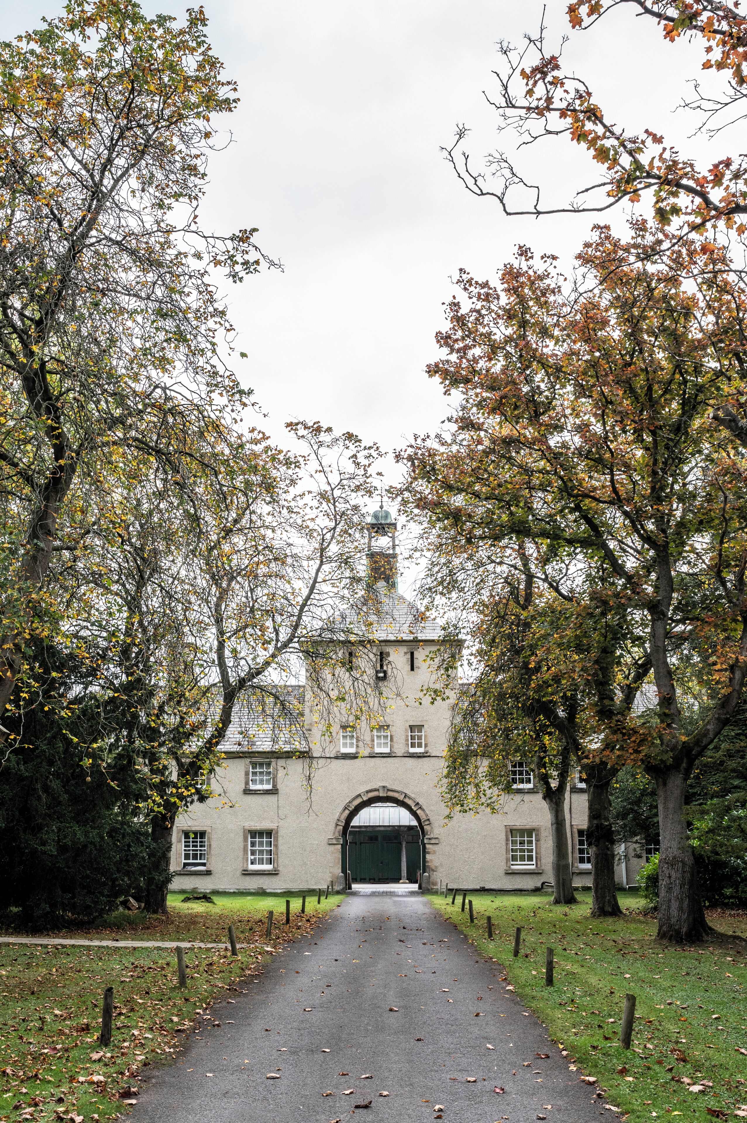 A pathway leading to a building with a large arched entrance, surrounded by trees with autumn foliage.