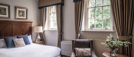 A neatly arranged hotel room with a large bed, a chair, a table with a vase of flowers, and a window with curtains.