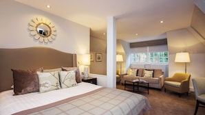 A hotel room with a large bed, a sofa, a chair, and a desk. There are multiple lamps and a mirror on the wall. - Crathorne Hall Hotel (Yarm)
