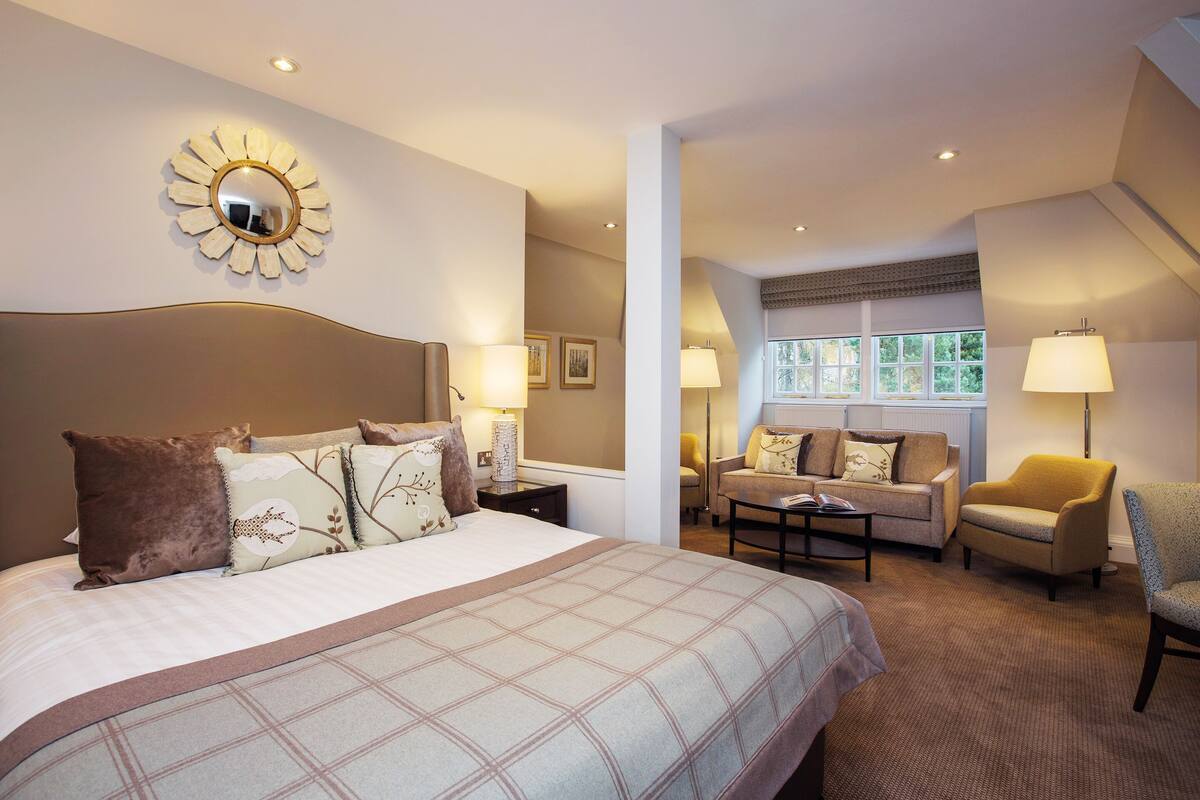 Quarto de hotel com uma cama grande, um sofá, uma poltrona e uma mesa de jantar.