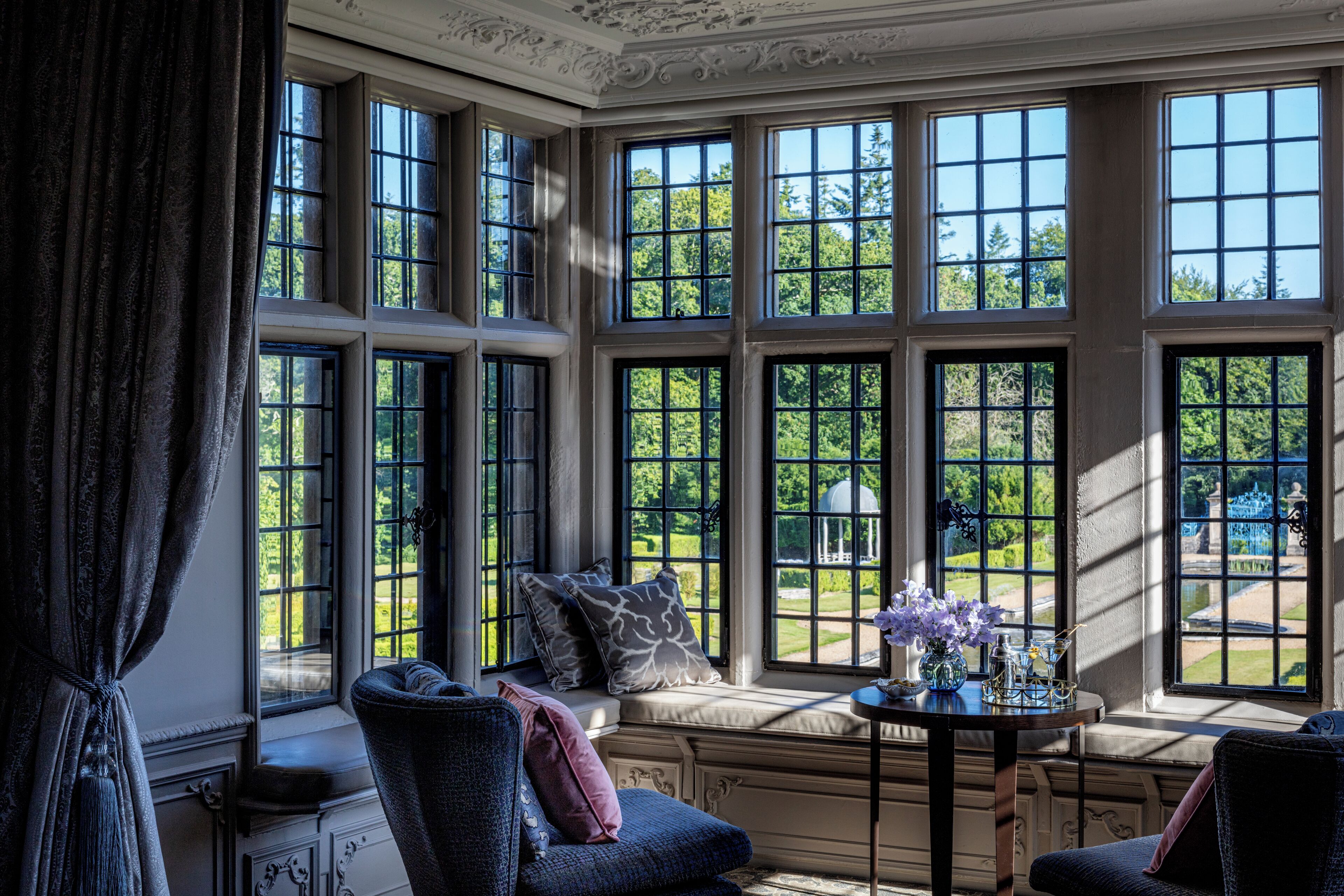 A room with large windows, a bench, and a small table with flowers.