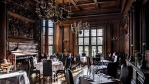 A formal dining room with multiple tables, elegant chandeliers, and a fireplace. - Rhinefield House Hotel (Brockenhurst)