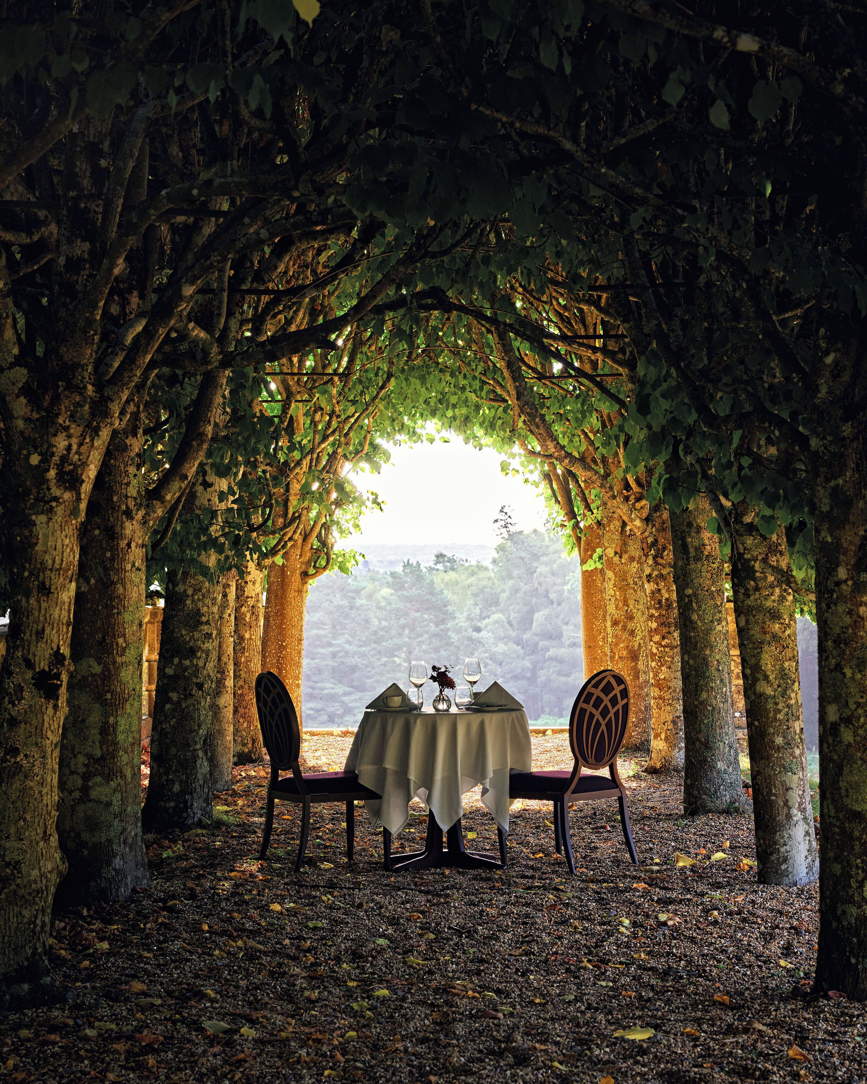 A table set for two under a natural archway with a view of a distant landscape.