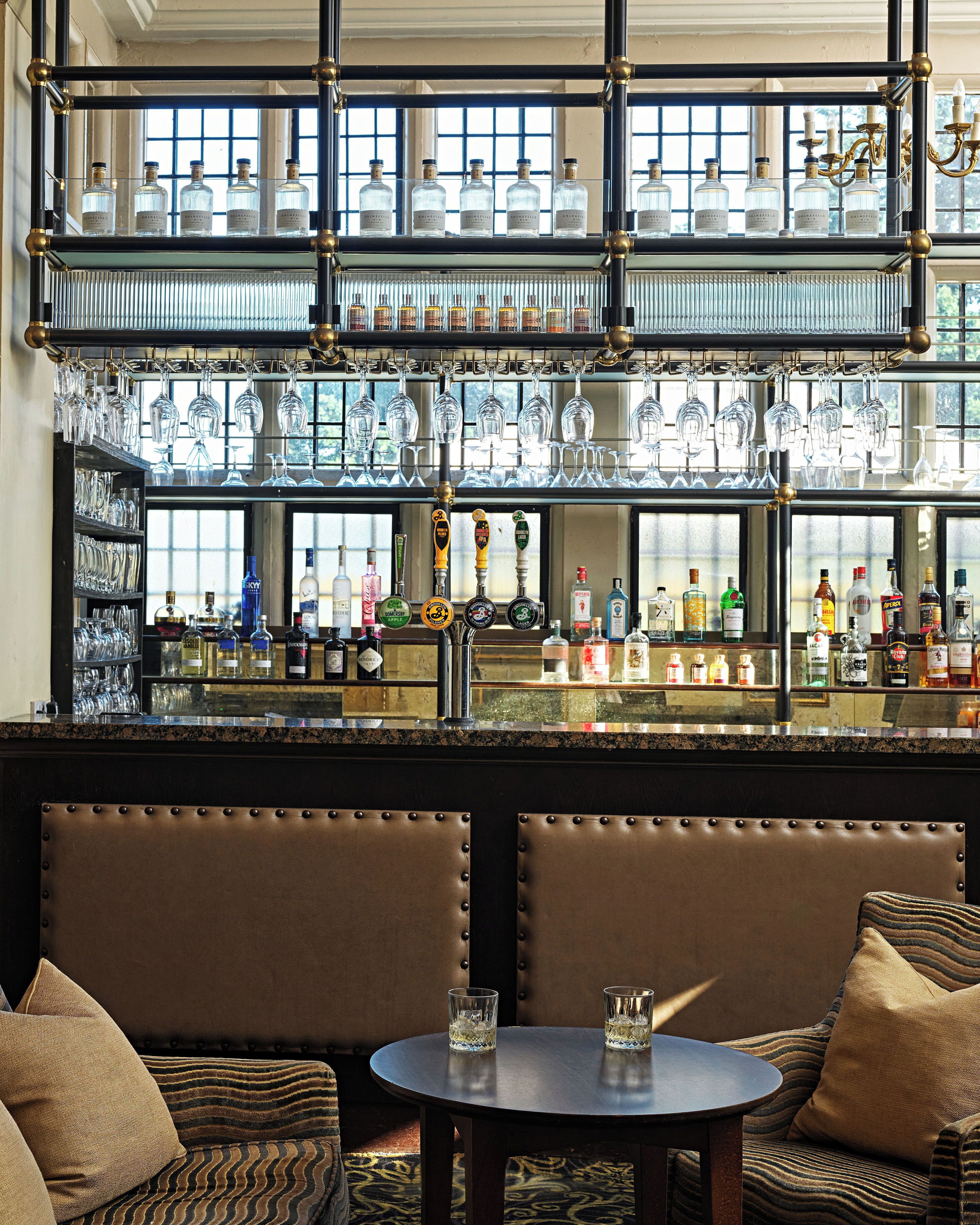 A bar area with multiple shelves of liquor bottles, a selection of glasses, and a seating area with a round table and cushioned chairs.