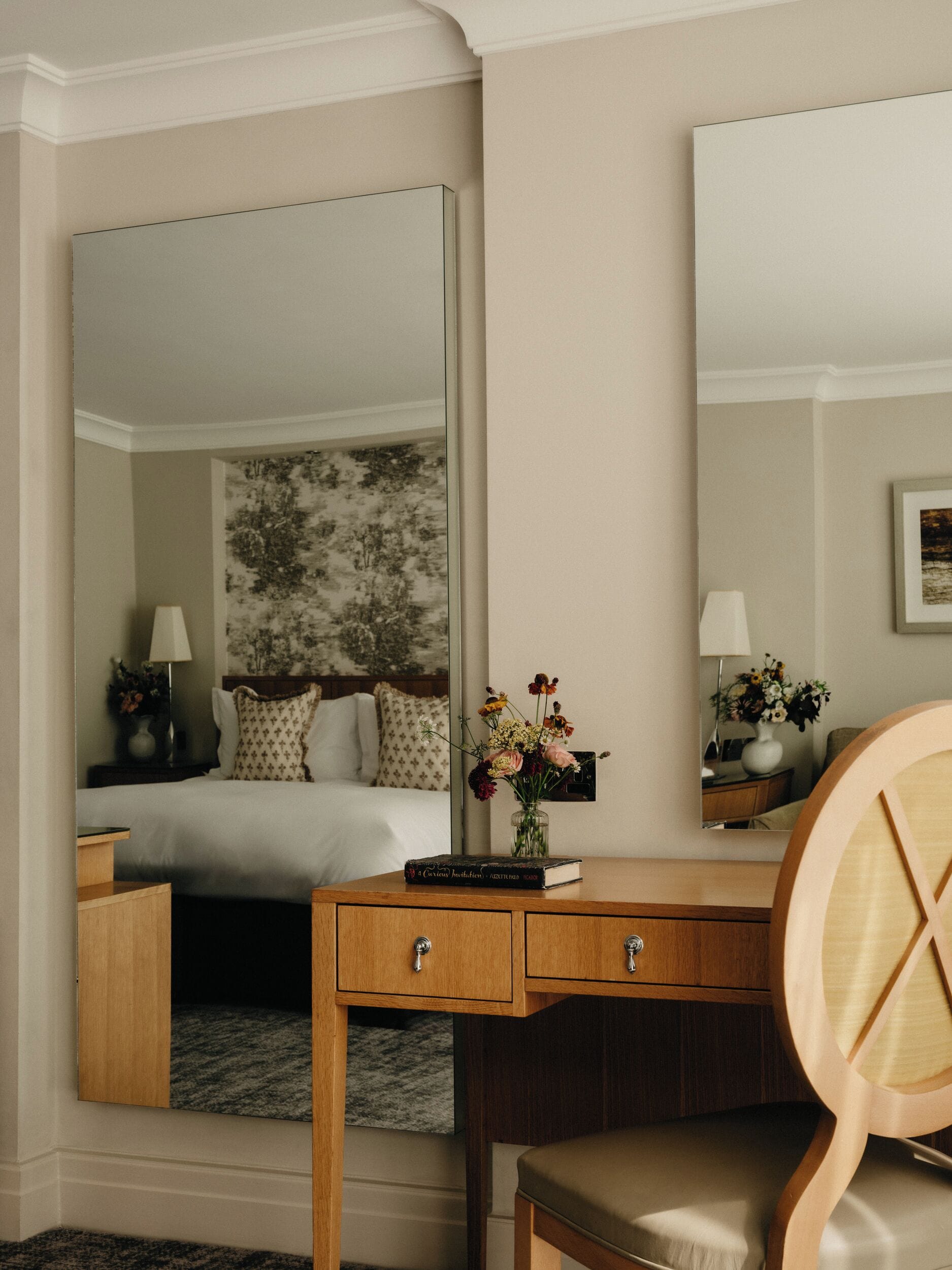 Ein Hotelzimmer mit einem Bett, einem Holztisch mit Schubladen, einem Stuhl, einem Spiegel und einer Vase mit Blumen.