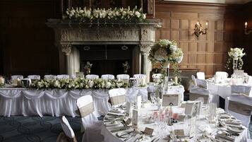 Un salón de banquetes con mesas dispuestas para un evento formal, con manteles blancos, centros de mesa florales y un ambiente a la luz de las velas.