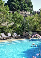 Una piscina con sillones de descanso y un edificio de piedra al fondo.