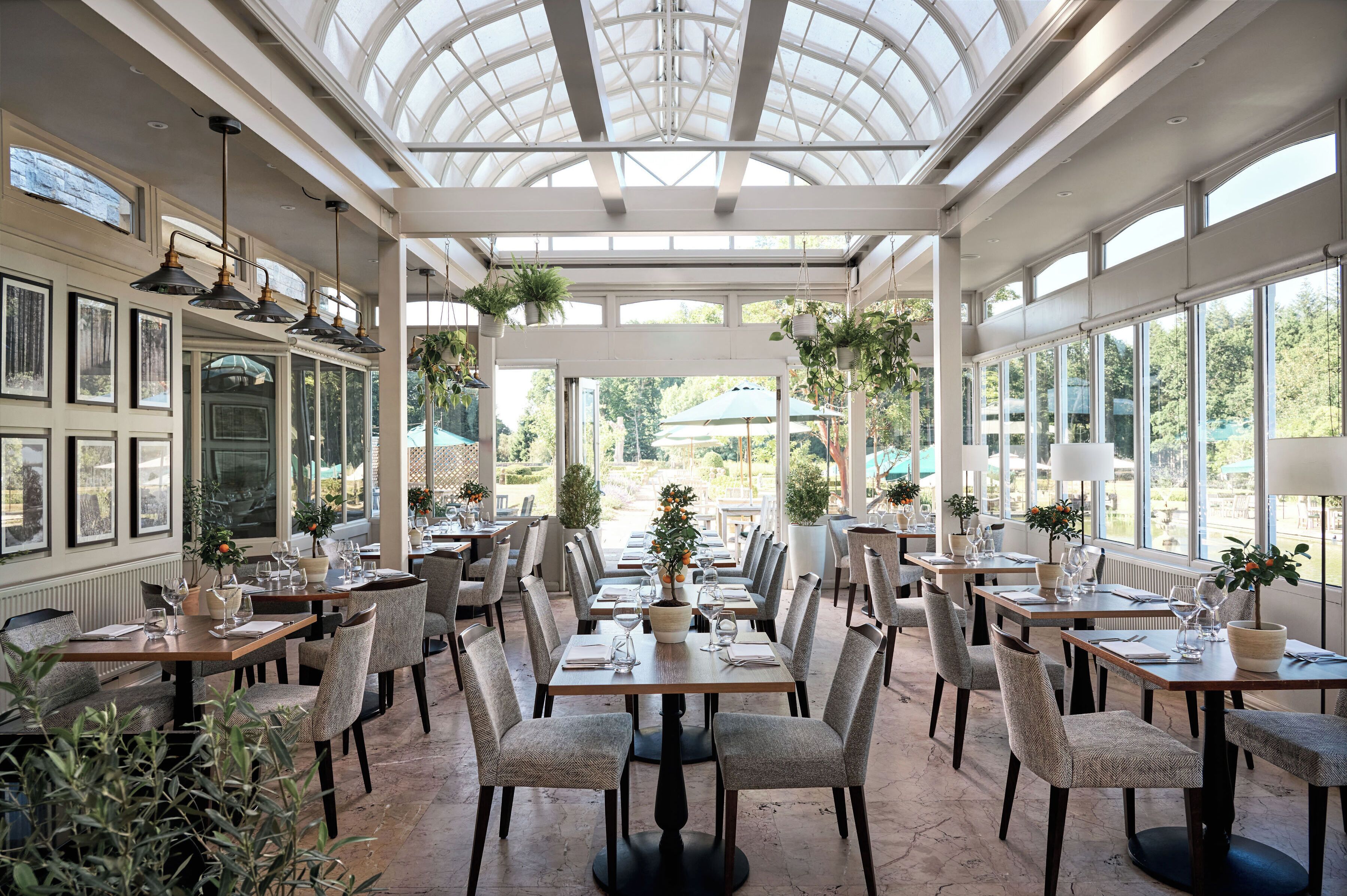 A conservatory with tables and chairs, framed pictures on the walls, and hanging plants.