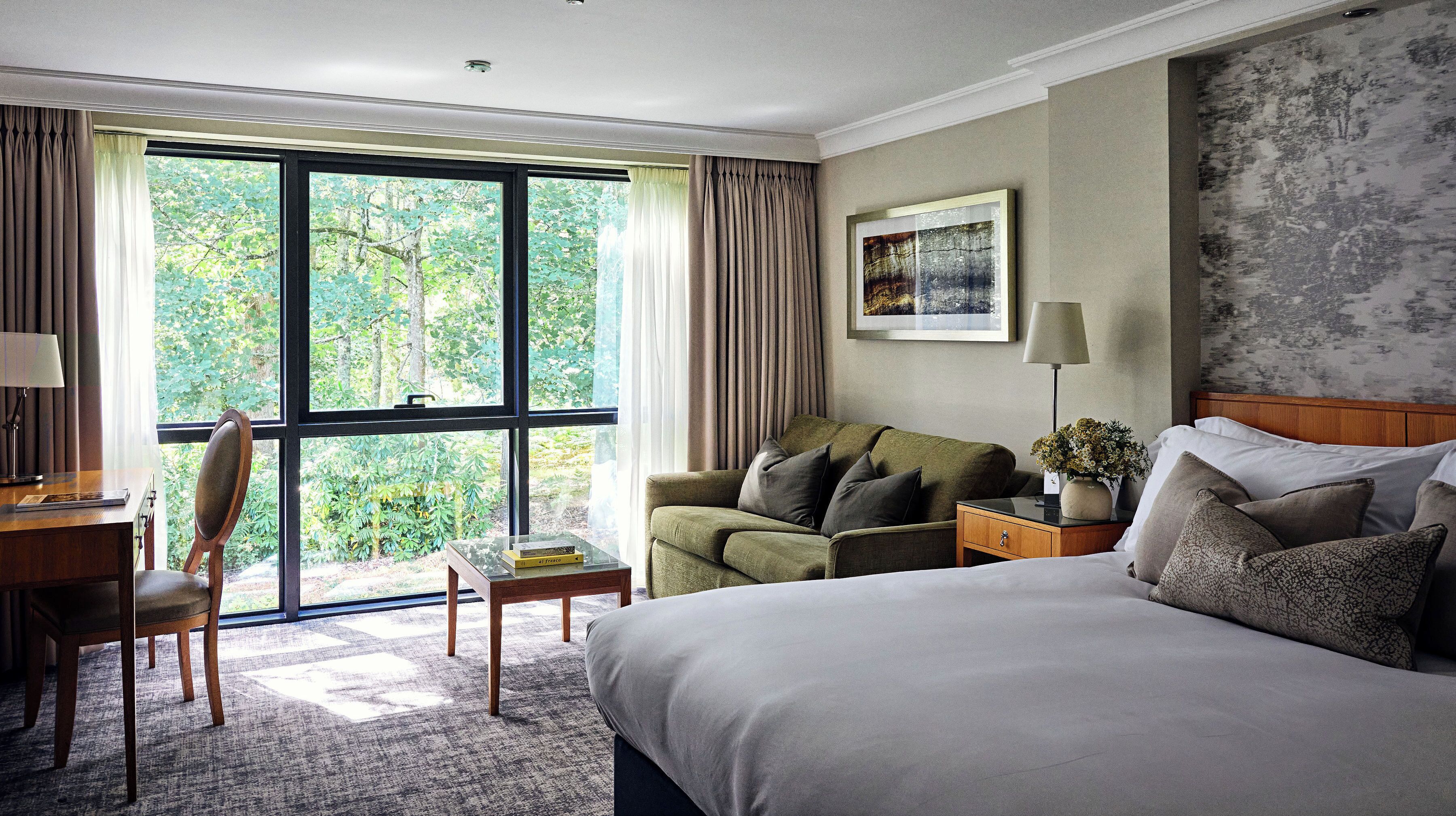 Habitación de hotel con cama, escritorio, silla, mesita de noche y ventana con cortinas.