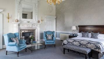 A bedroom with a large bed, two armchairs, a fireplace, and a chandelier.