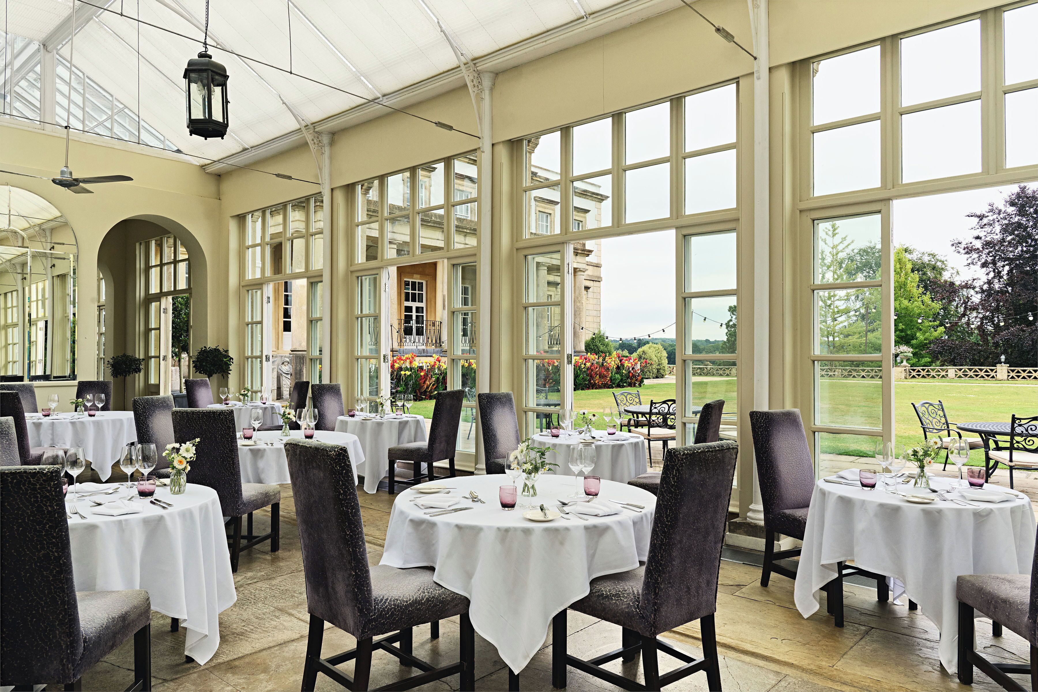 A restaurant with round tables, chairs, and a view of a garden.