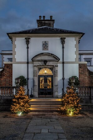 A building with a symmetrical facade, a central entrance with a decorative arch, and two illuminated Christmas trees. - Buxted Park Hotel (Uckfield)