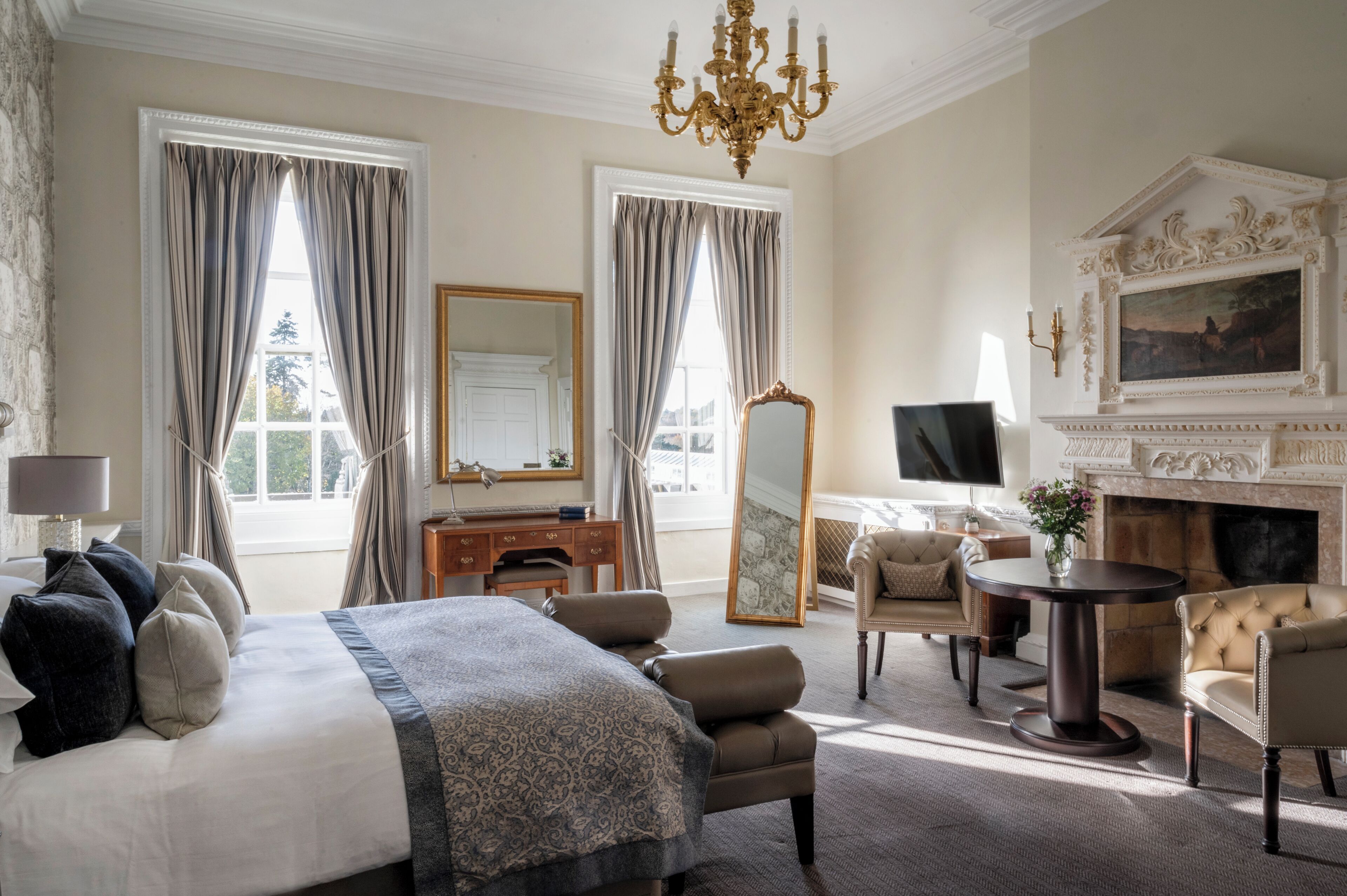 A hotel room with a large bed, a sitting area with a fireplace, a television, and a mirror.