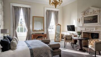 A hotel room with a large bed, a sitting area with a fireplace, a television, and a mirror.