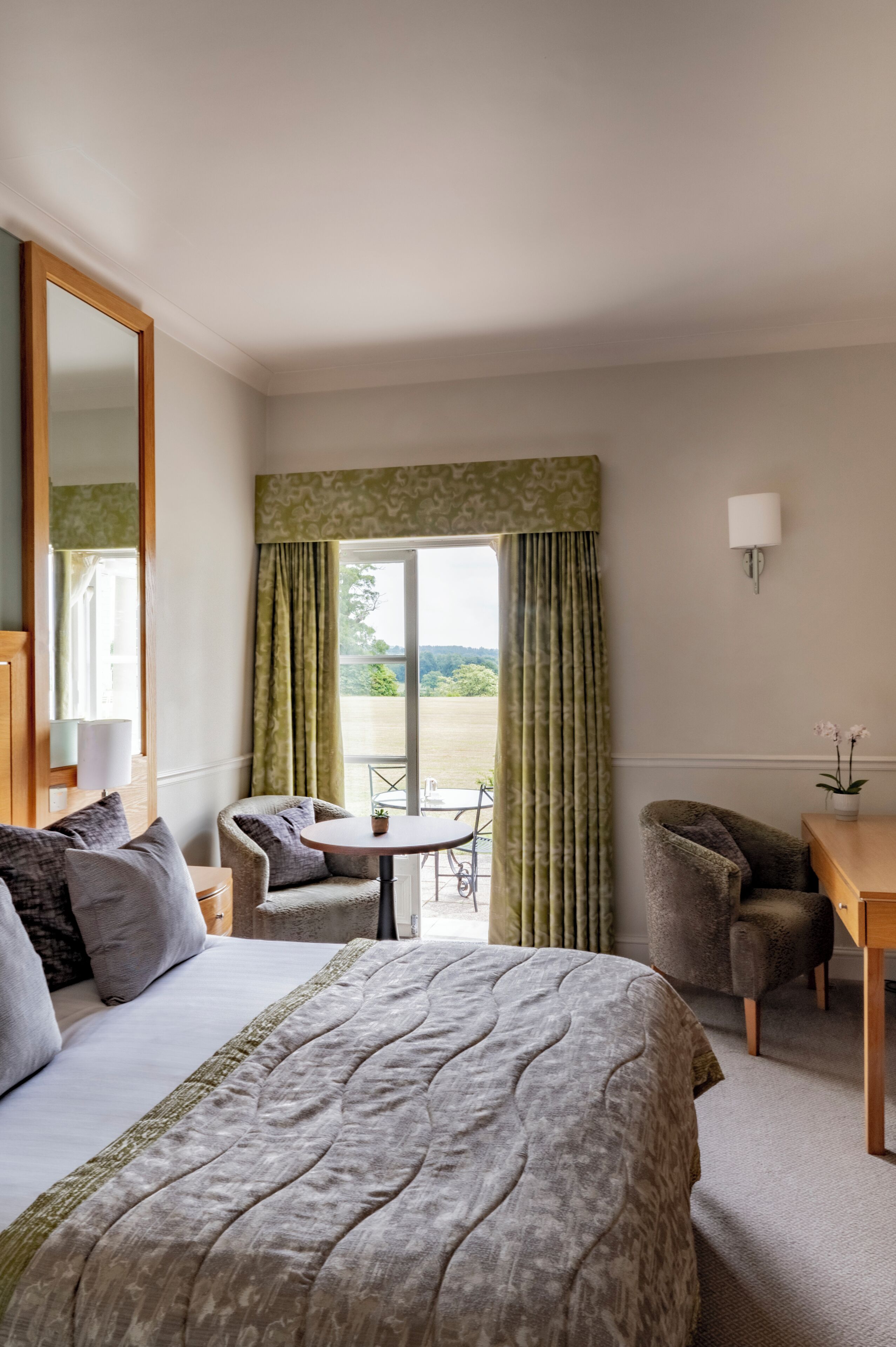 A hotel room with a large bed, a sitting area with a table and chairs, a desk, and a view of the outdoors.