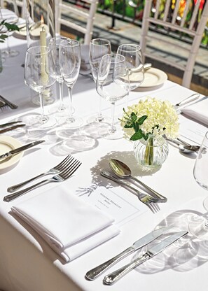 A table set for a wedding breakfast with a menu, silverware, and a vase of white flowers. - Buxted Park Hotel (Uckfield)