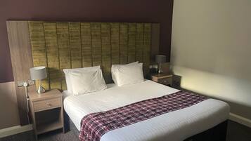 A hotel room with a large bed, two bedside tables, a headboard, and a carpeted floor.