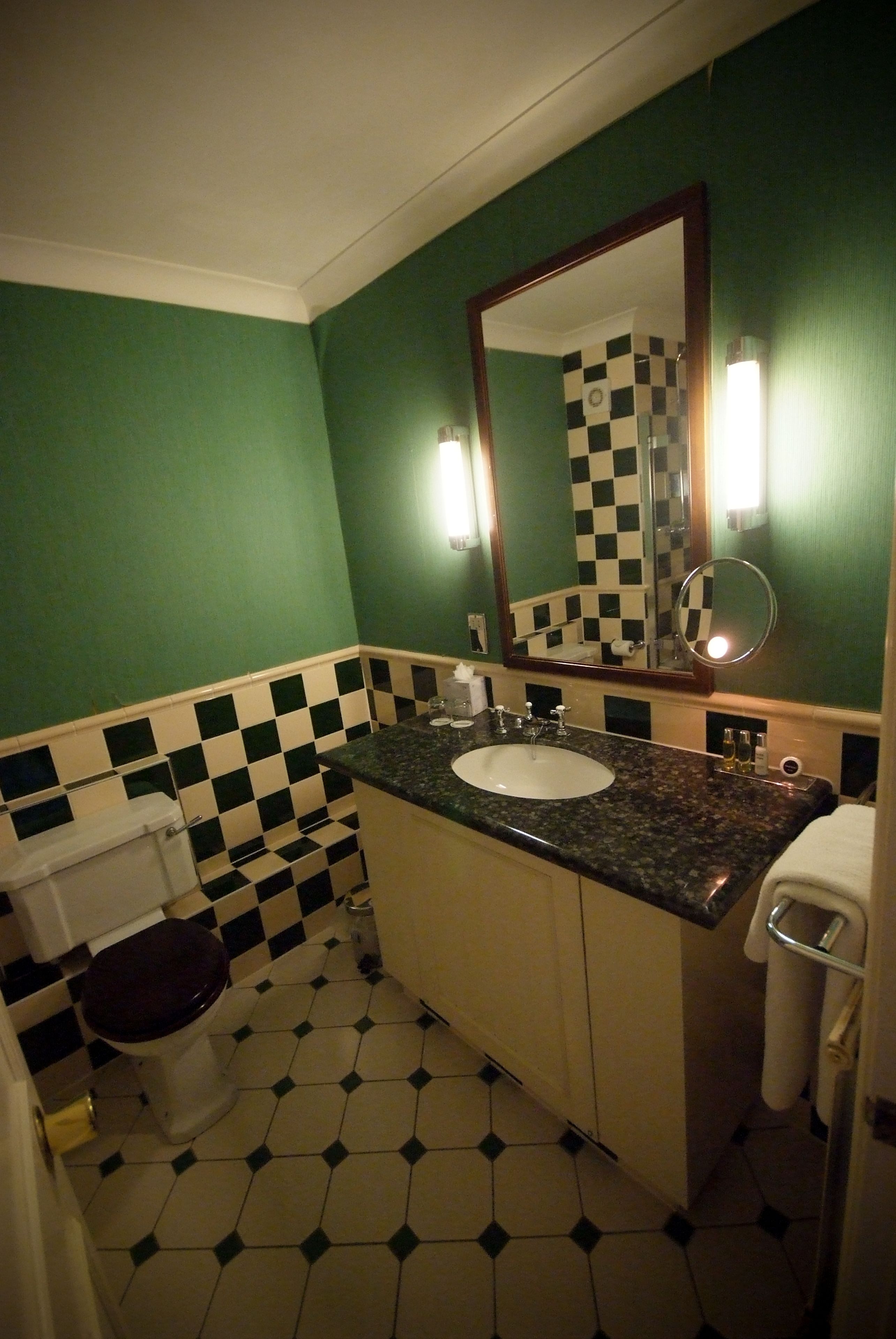 A bathroom with a checkered floor, green walls, a sink with a mirror, and a toilet.