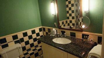 A bathroom with a checkered floor, green walls, a sink with a mirror, and a toilet.