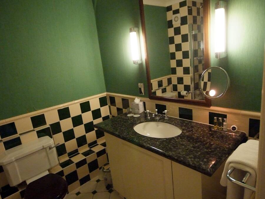 A bathroom with a checkered floor, green walls, a sink with a mirror, and a toilet.
