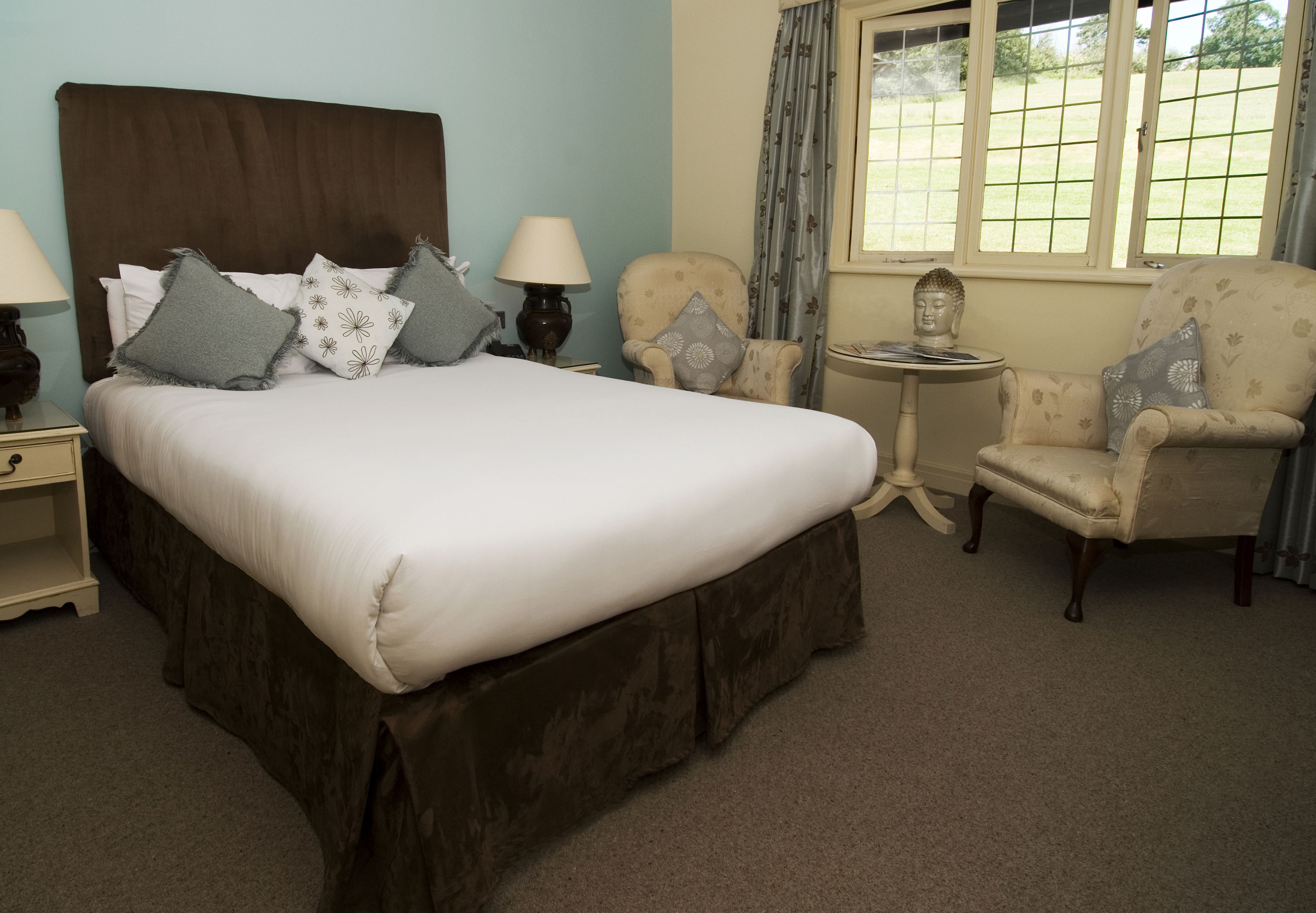 A neatly arranged bedroom with a large bed, two chairs, a small table, and a window with a view.