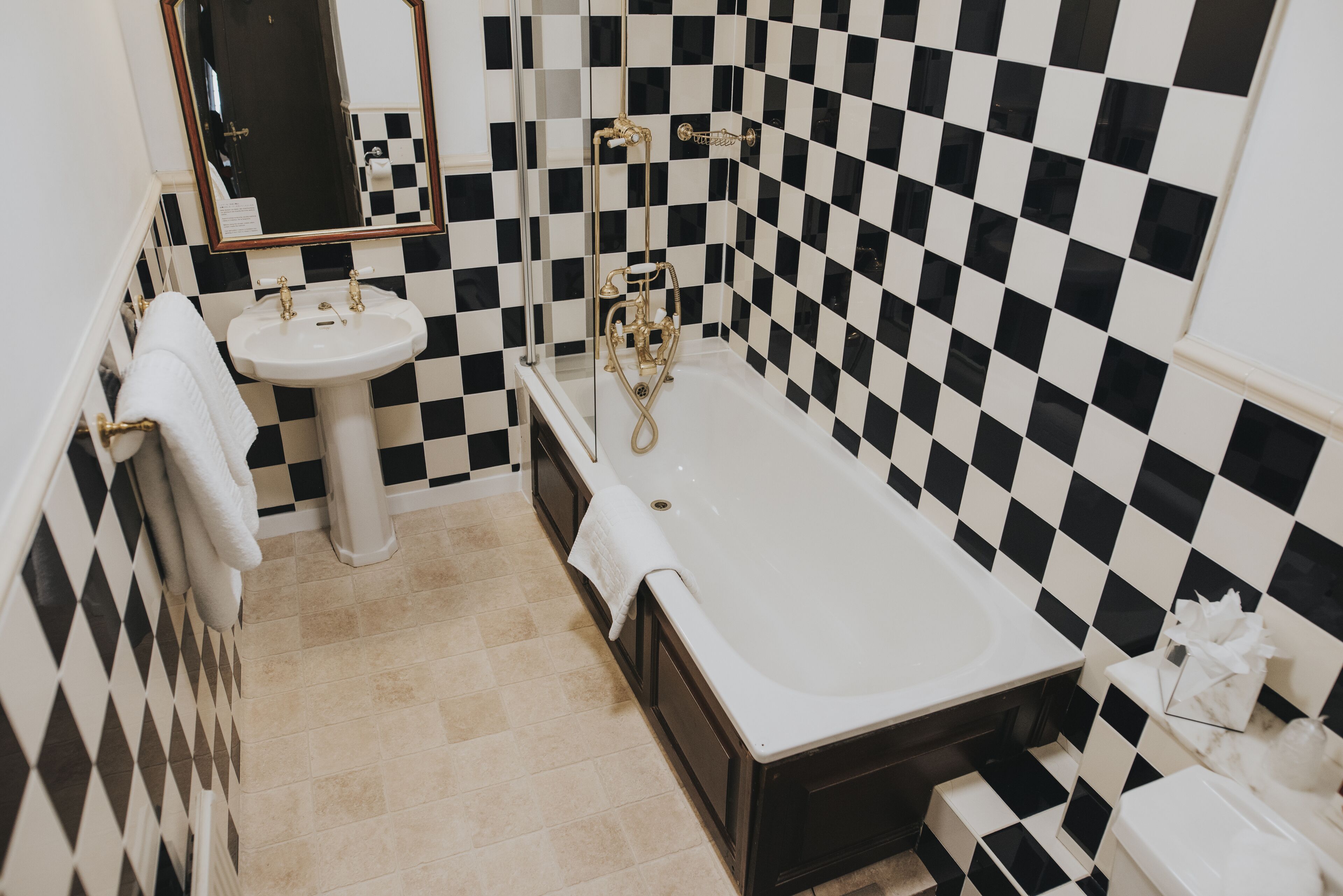 Un baño con pared de baldosas blancas y negras en damero, un lavamanos blanco y una bañera.