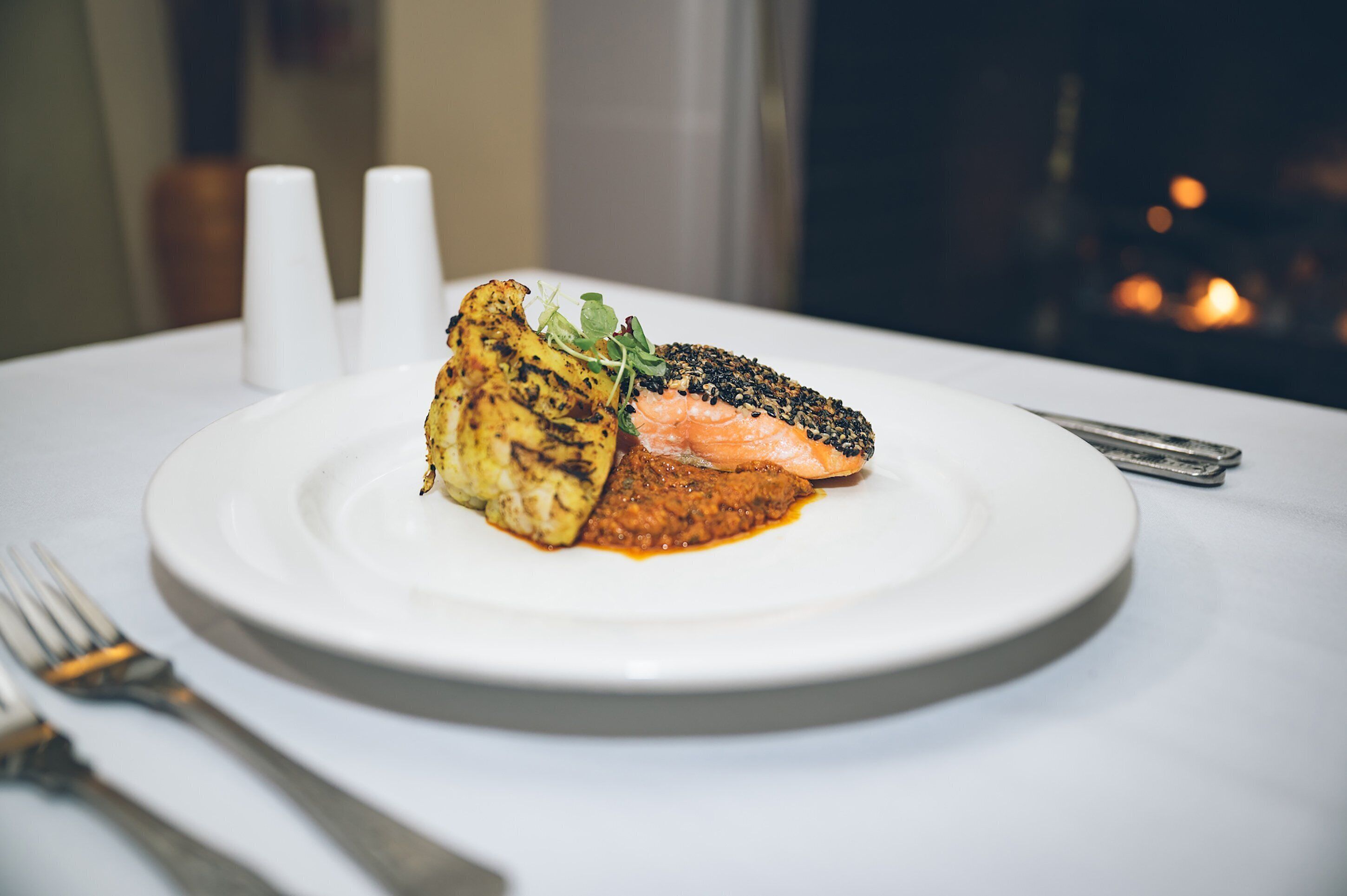 Une assiette de nourriture comprenant du poulet grillé et du saumon, agrémentée de jeunes pousses, sur une assiette blanche.