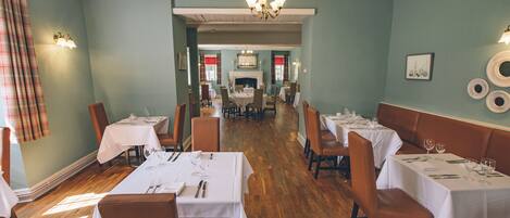 A dining area with tables set for a meal, a fireplace, and a chandelier.