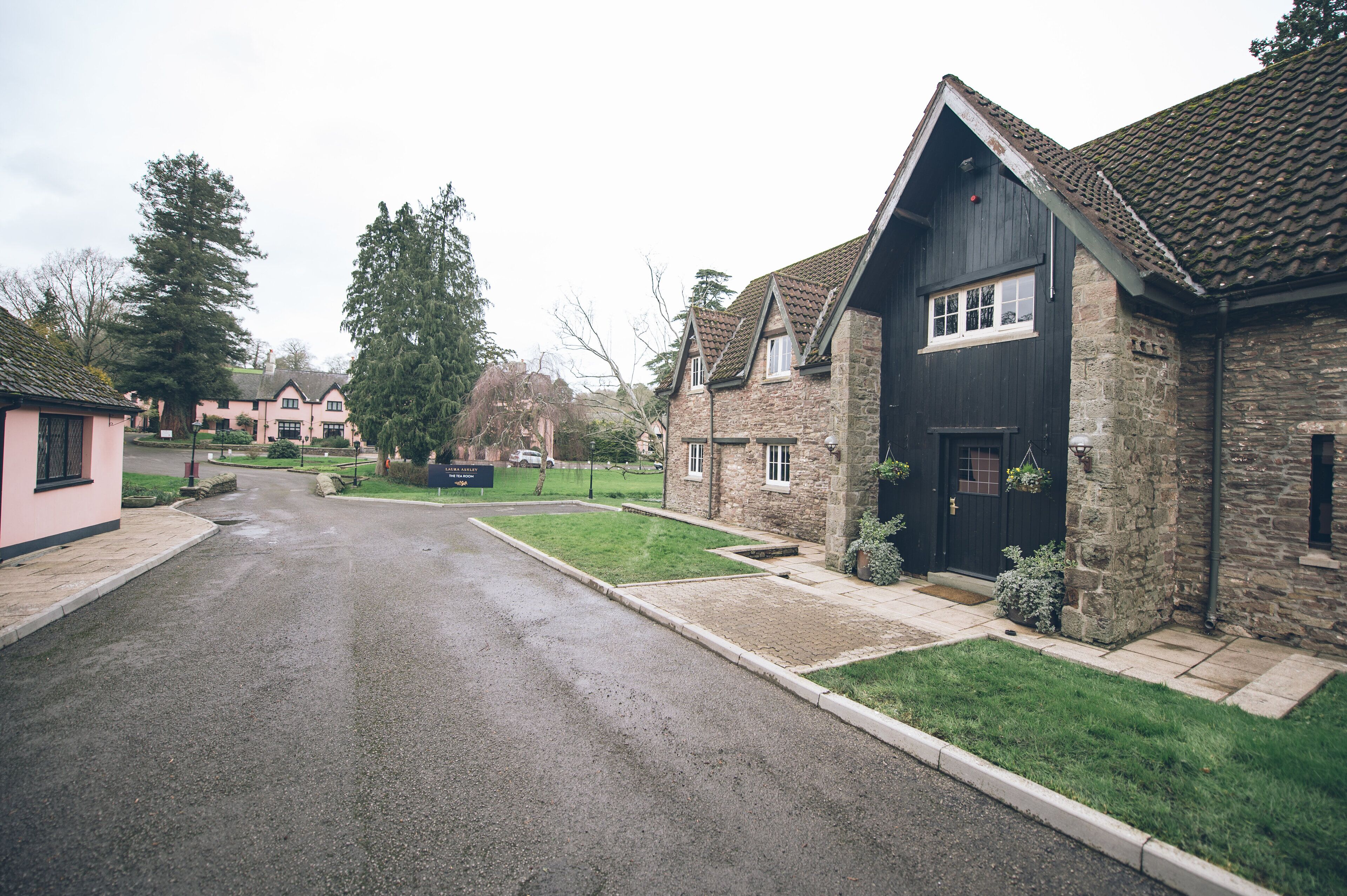 A residential street with houses, including a stone building with a dark roof and a pink house.