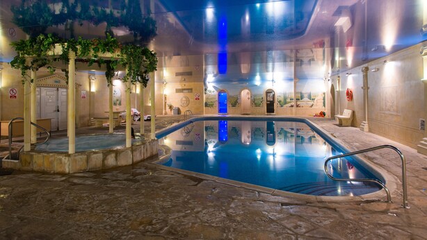 An indoor swimming pool with a stone floor, surrounded by columns and a covered area with greenery. - Cwrt Bleddyn Hotel & Spa (Usk)
