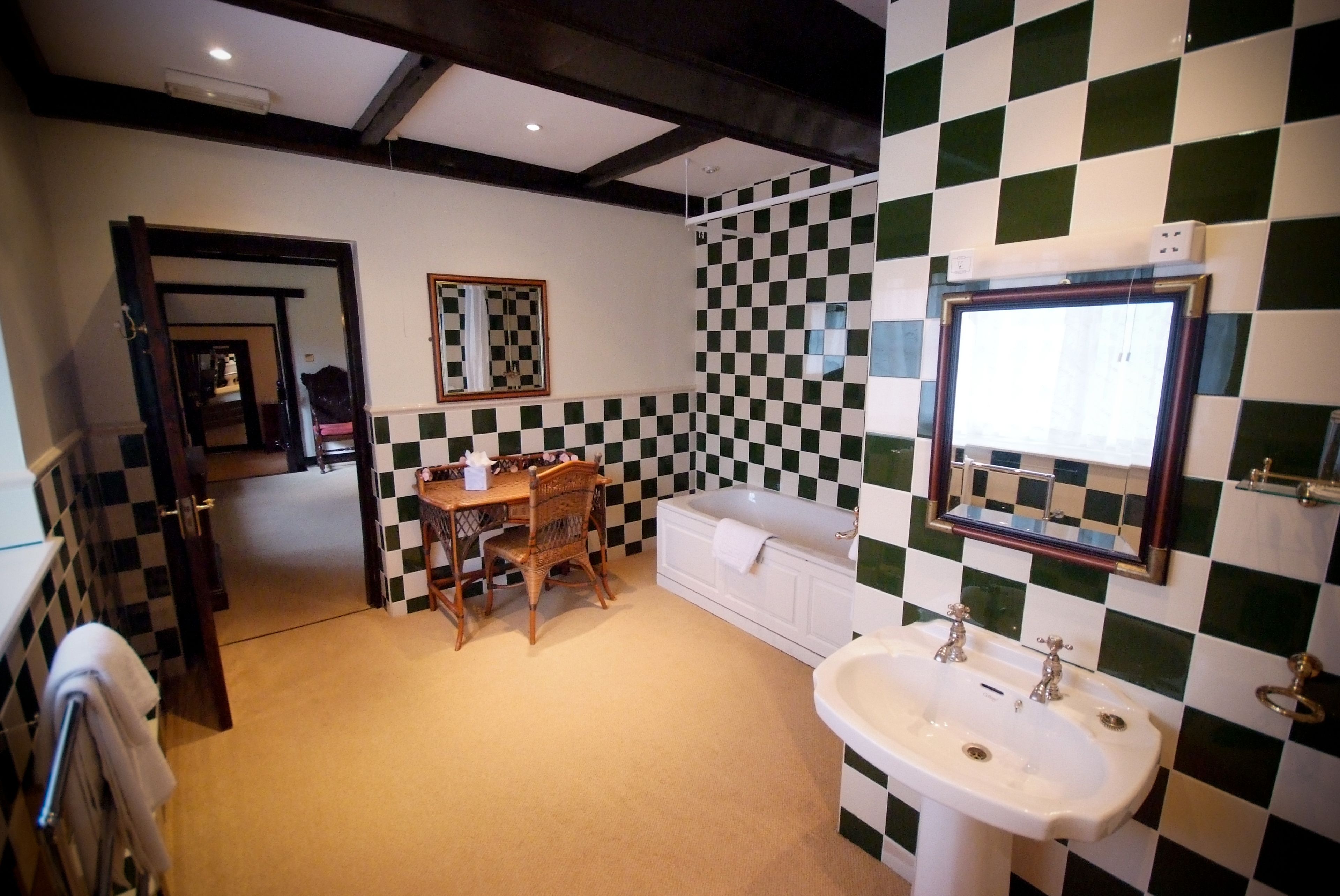 A bathroom with a checkered tile wall, a sink, a bathtub, and a wooden table with chairs.