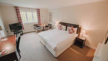 A hotel room with a large bed, a desk with a chair, a television, and a window with curtains.
