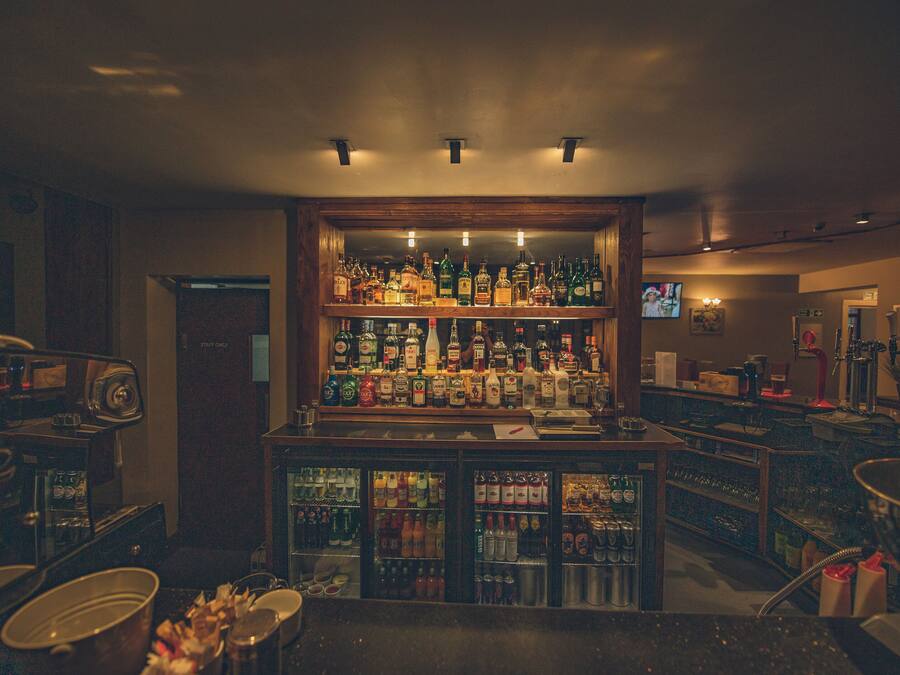 Baaritiskialue, jossa on hyllyjä täynnä alkoholijuomapulloja, televisioruutu ja kahvinkeitin.