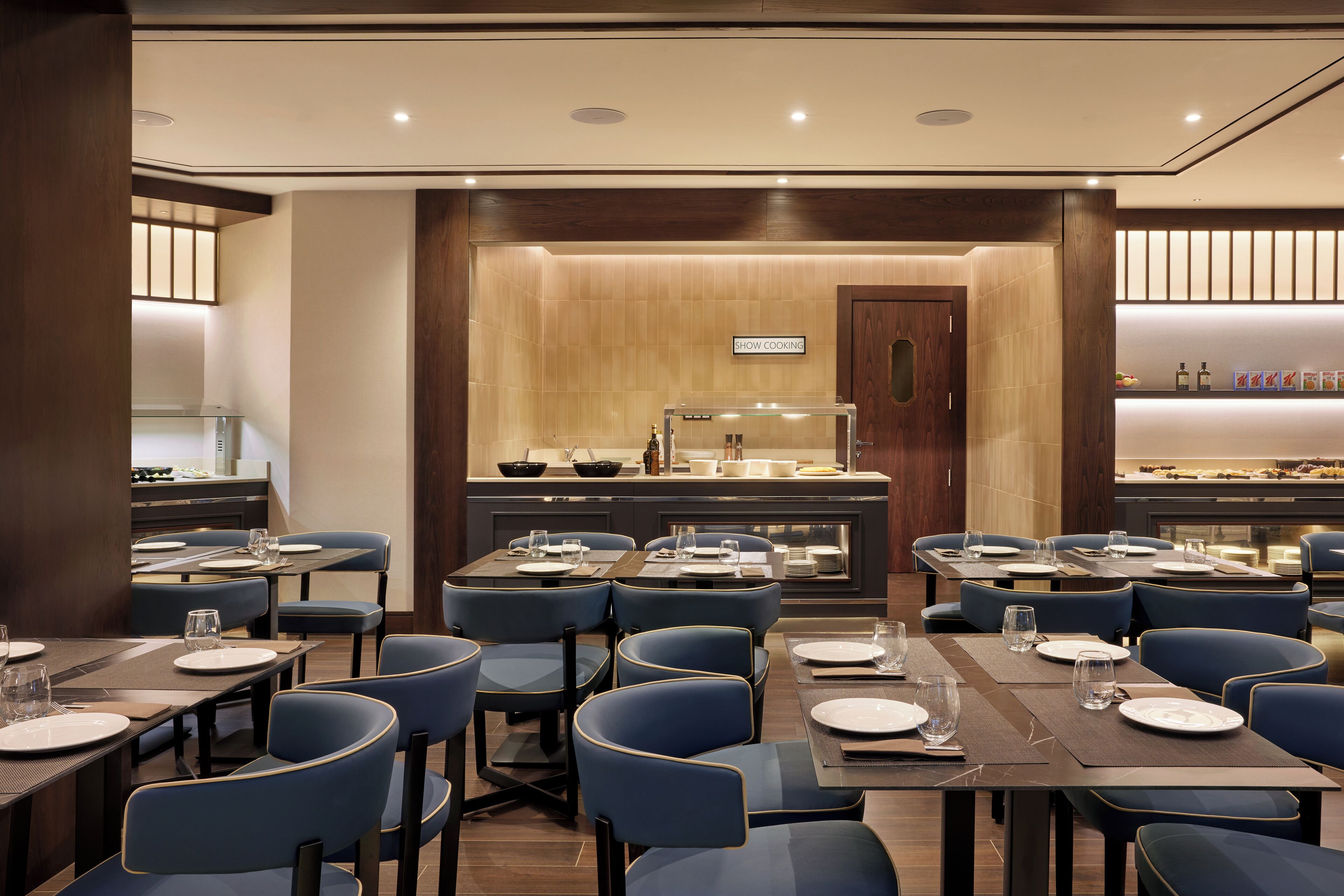 Un restaurant doté de plusieurs tables et chaises, d’un espace cuisine et d’un buffet.