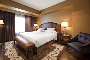 Ein Hotelzimmer mit einem großen Bett, einer Bank, einem Sessel, einem Nachttisch und einer Lampe.