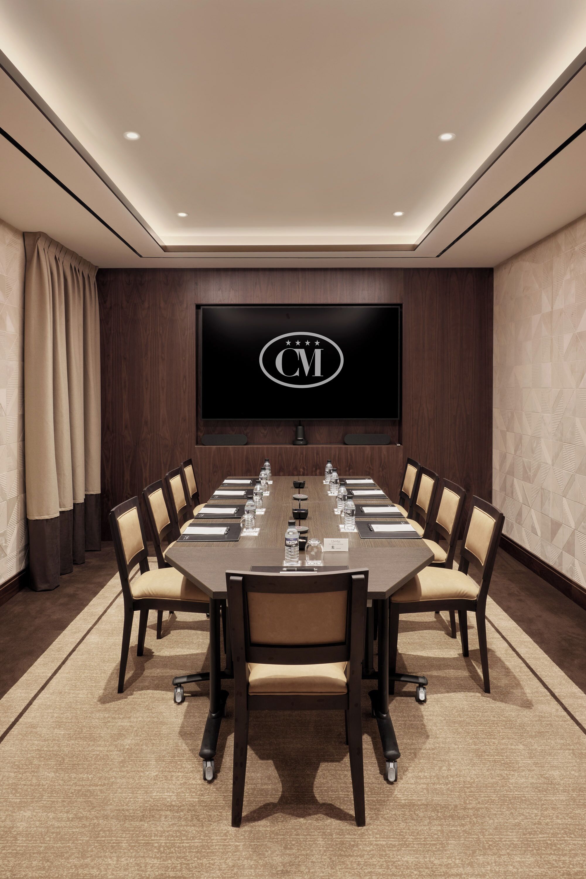 Un salón de conferencias con una larga mesa, sillas, un televisor de pantalla plana y un logotipo en la pared.