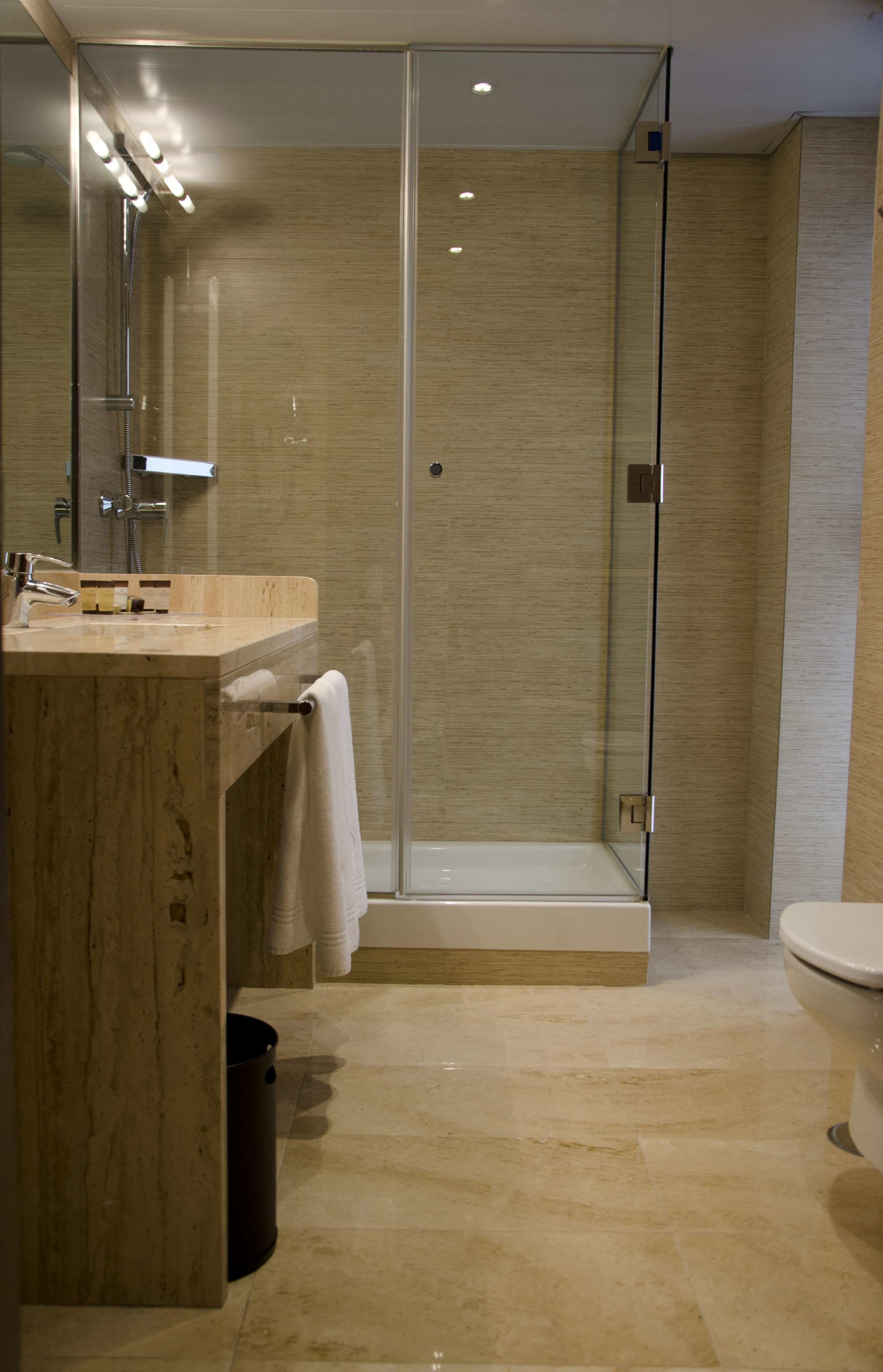 A modern bathroom with a glass-enclosed shower, a marble sink, and a toilet.